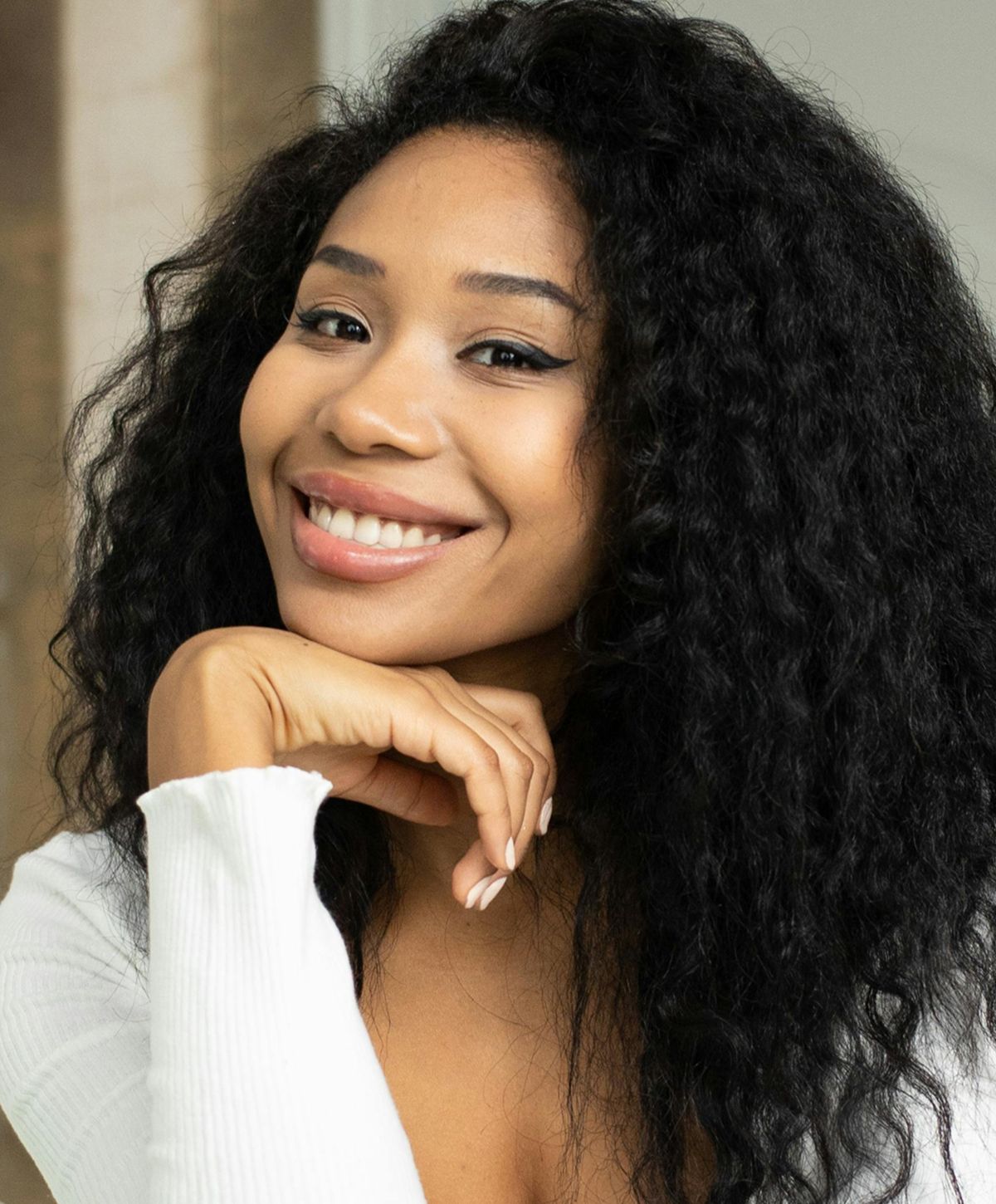 Smiling woman with curly hair resting chin on hand.