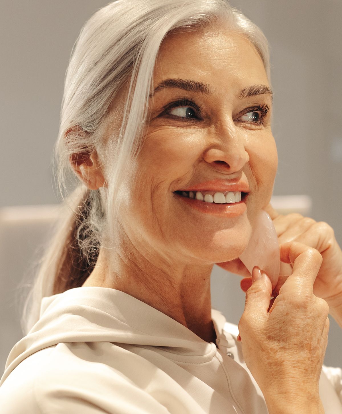 Woman smiling while using skincare tool on cheeks.