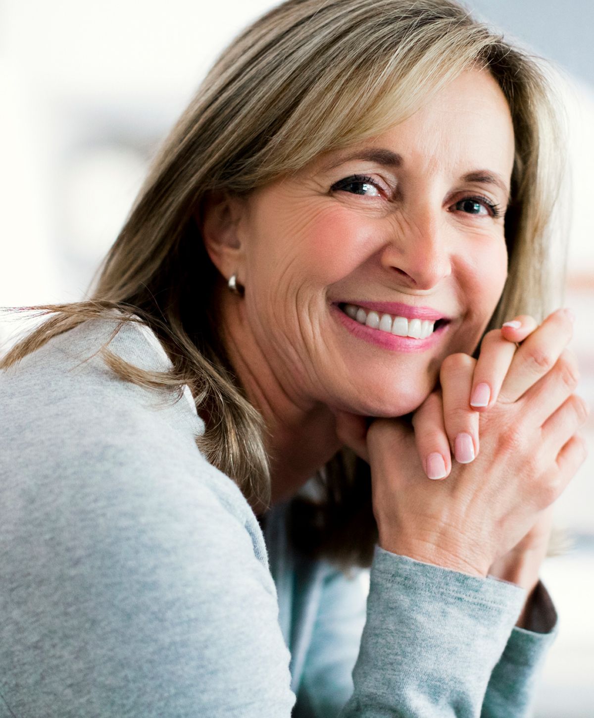 Smiling woman with hands clasped near face.