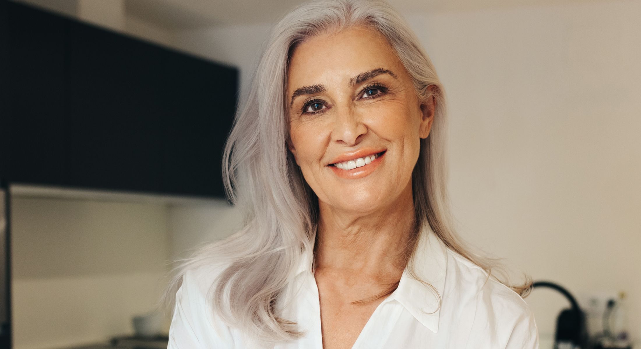Smiling woman with long gray hair indoors.