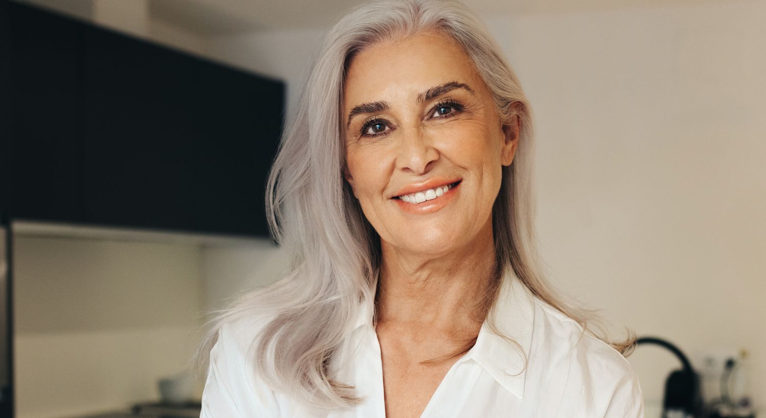 Smiling woman with silver hair in kitchen.