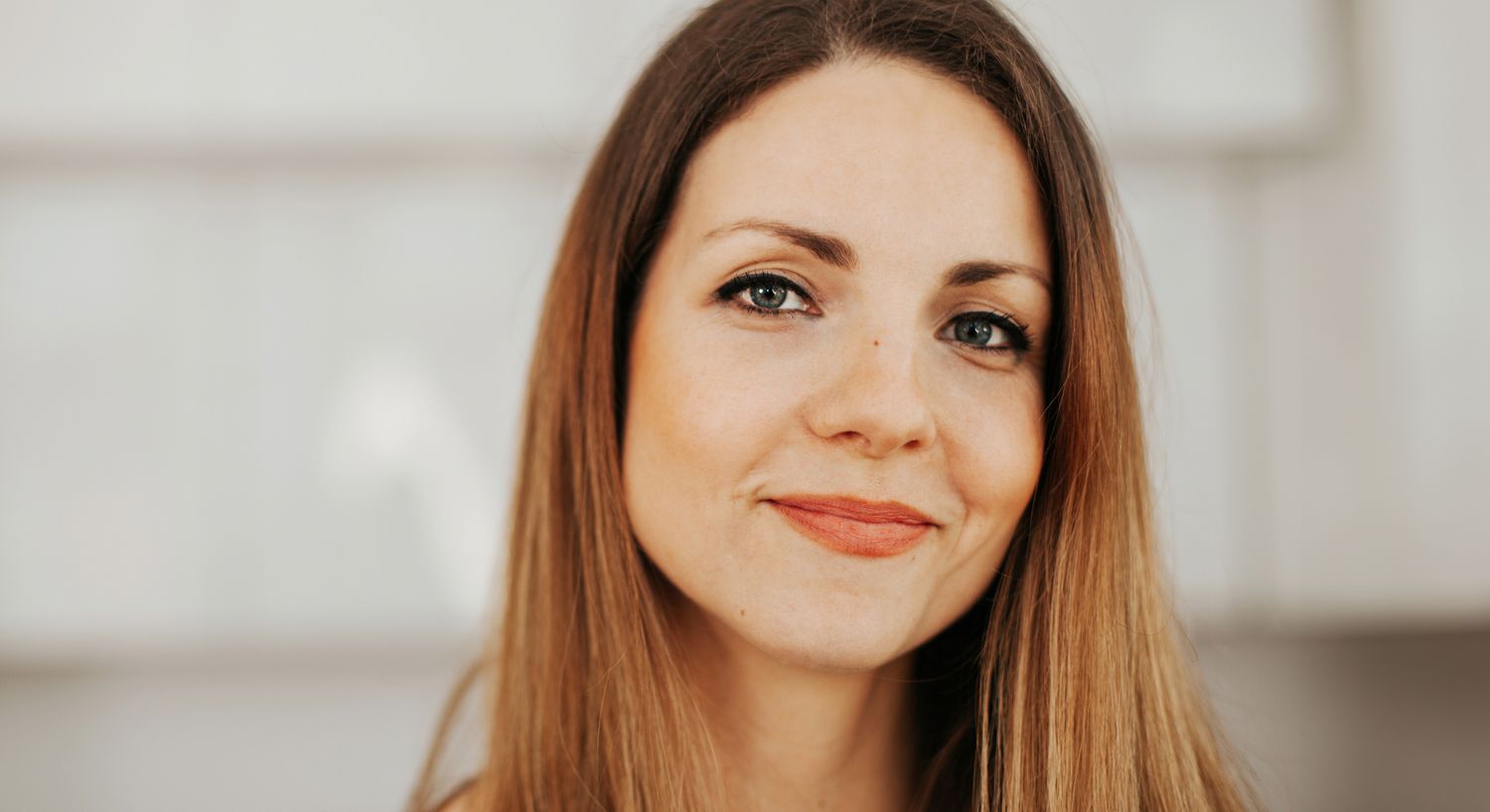 Smiling woman with long brown hair indoors.