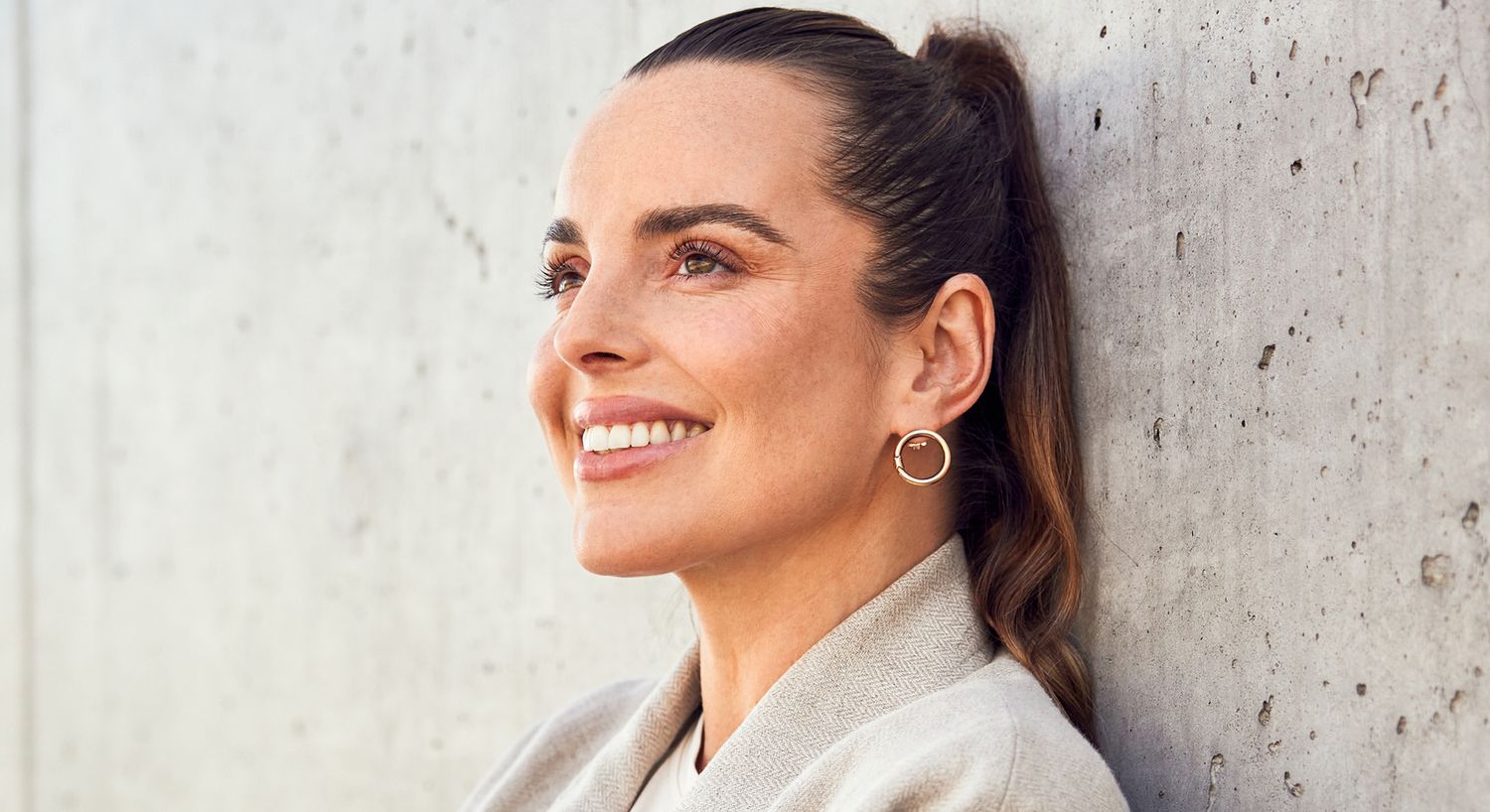Smiling woman leaning against a concrete wall.