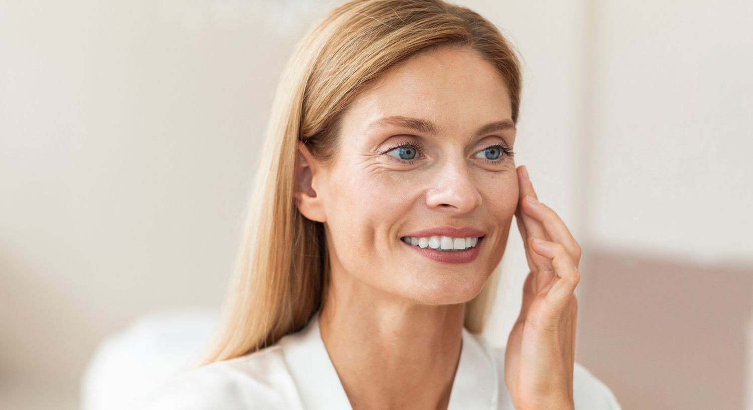 Woman smiling while applying skincare product.