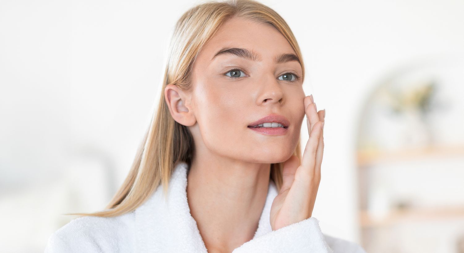 Woman applying skincare routine in bright bathroom.